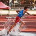 Male athlete running through water splash on track field during steeplechase event.